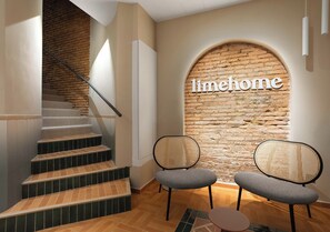 A staircase leading to a room with a brick wall and the word 'limehome' on it. There are two chairs and a small table in the room. - Limehome Valencia d'Ernest Anastasio  (València)