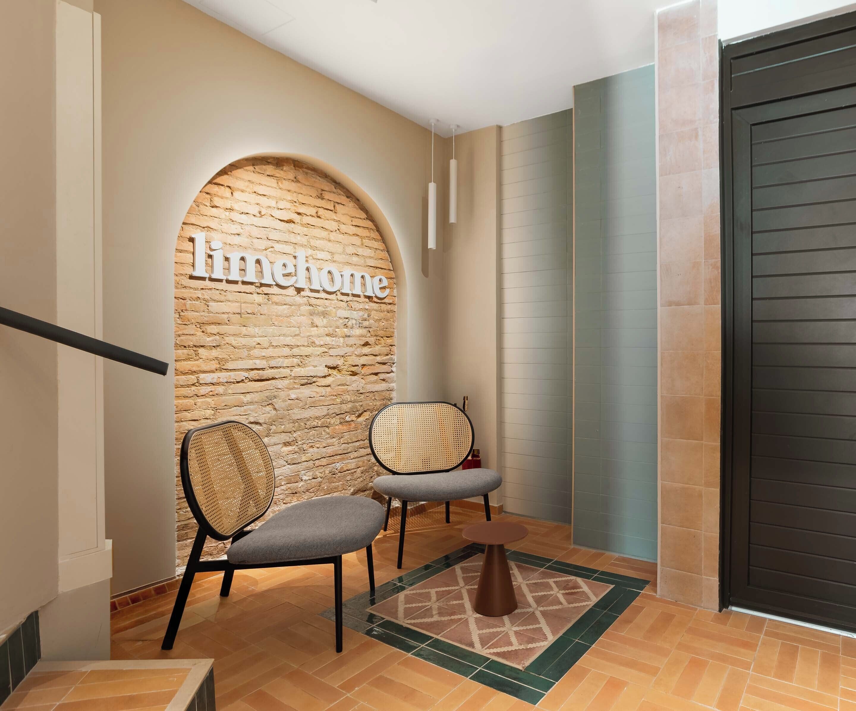 A hallway with a brick wall, two chairs, a small rug, and a door.