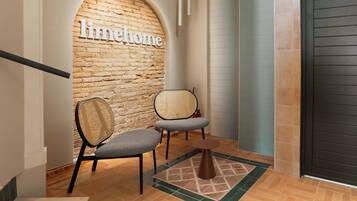 A hallway with a brick wall, two chairs, a small rug, and a door.