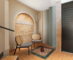 A hallway with a brick wall, two chairs, a small rug, and a door. - Limehome Valencia d'Ernest Anastasio  (València)