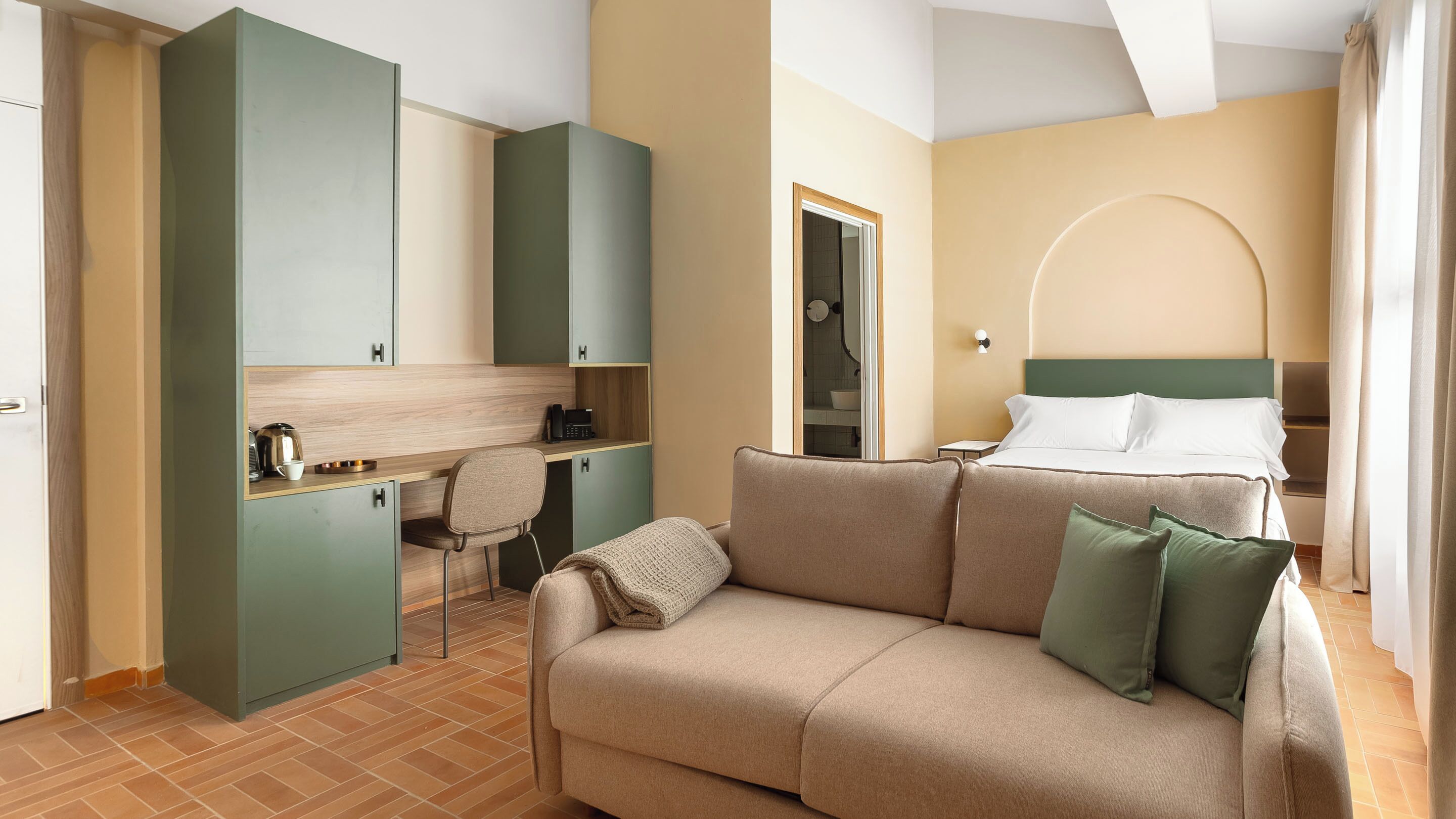 A hotel room with a bed, a sofa, a desk, and a shower area.