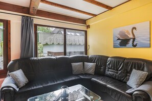 Un sofá de cuero negro con cojines estampados, una mesa de centro de vidrio con un control remoto y un cuadro de un cisne en la pared.
