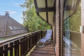 Una terraza de madera con dos sillones reclinables a rayas, un ventanal y vista a una casa con techo de tejas.
