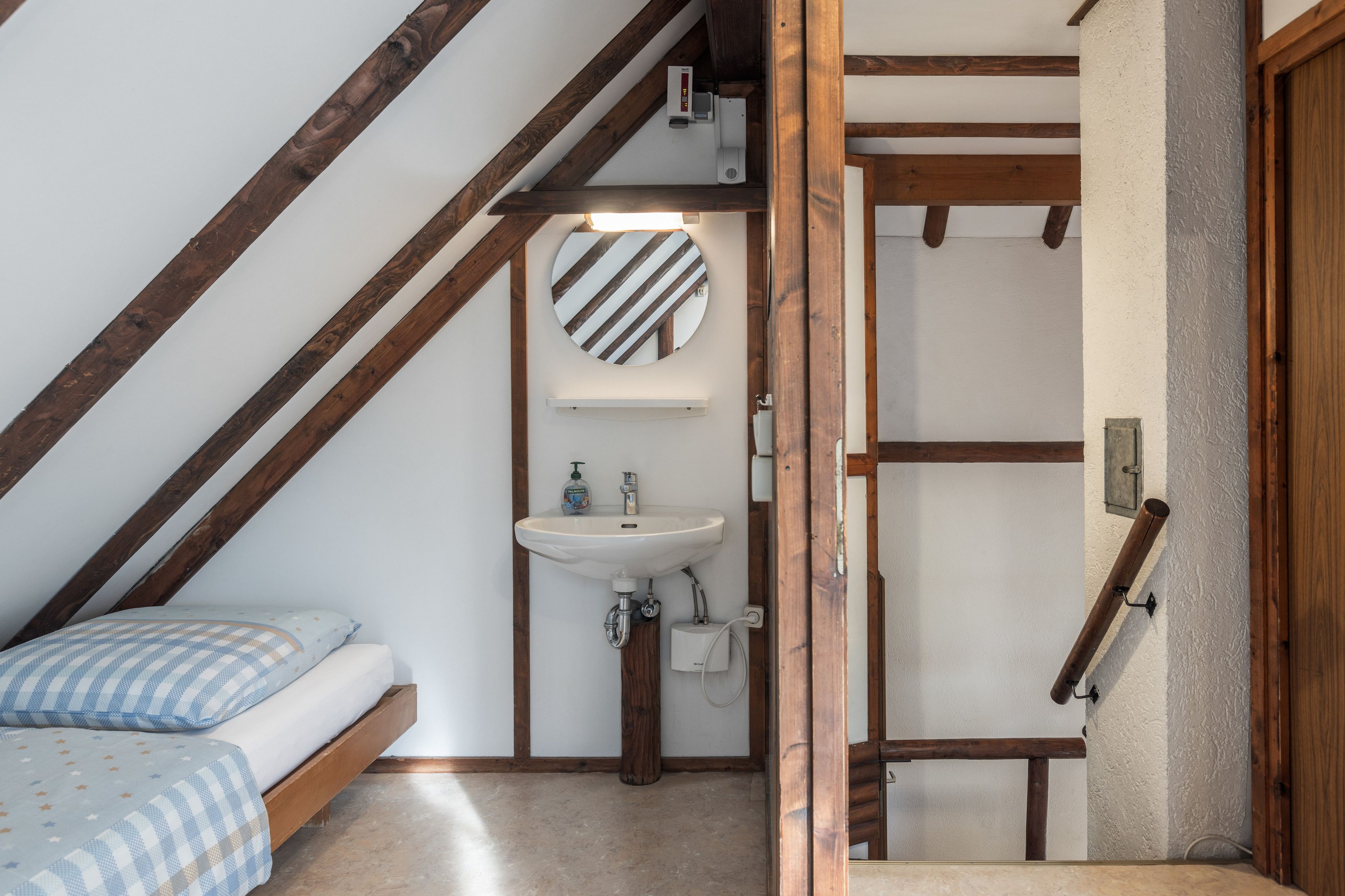 Une petite chambre à coucher accueillante, avec un lit, un miroir rond et un lavabo intégré.