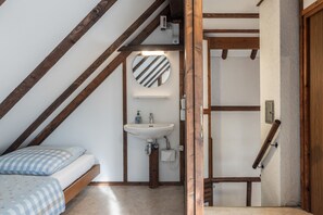 Une petite chambre à coucher accueillante, avec un lit, un miroir rond et un lavabo intégré.