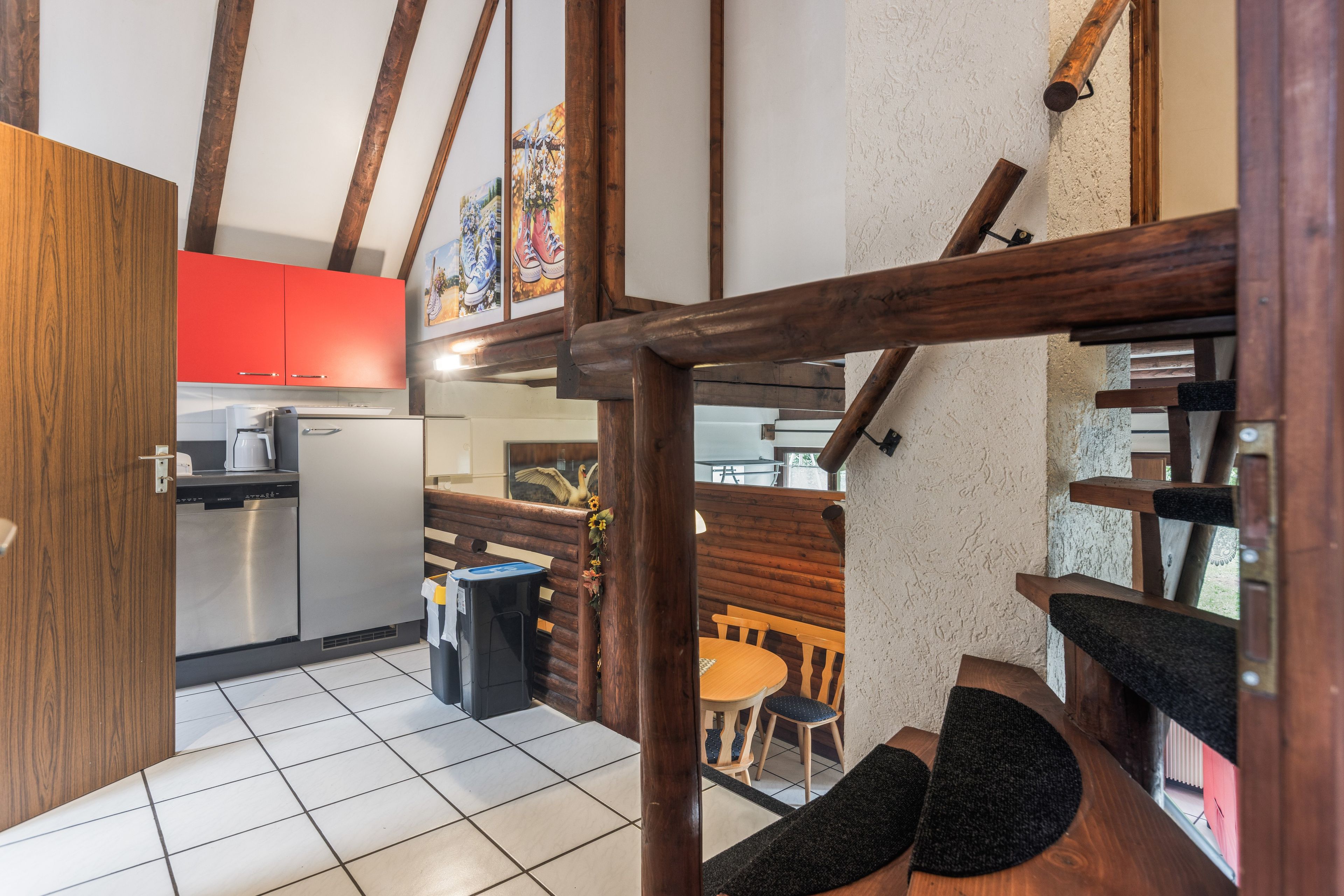 A kitchen with modern appliances, a dining area with wooden furniture, and a staircase with exposed wooden beams.