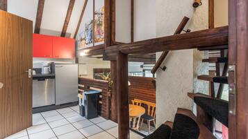A kitchen with modern appliances, a dining area with wooden furniture, and a staircase with exposed wooden beams.