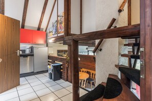 Una cocina con electrodomésticos modernos, un comedor con mobiliario de madera y una escalera con vigas de madera a la vista.