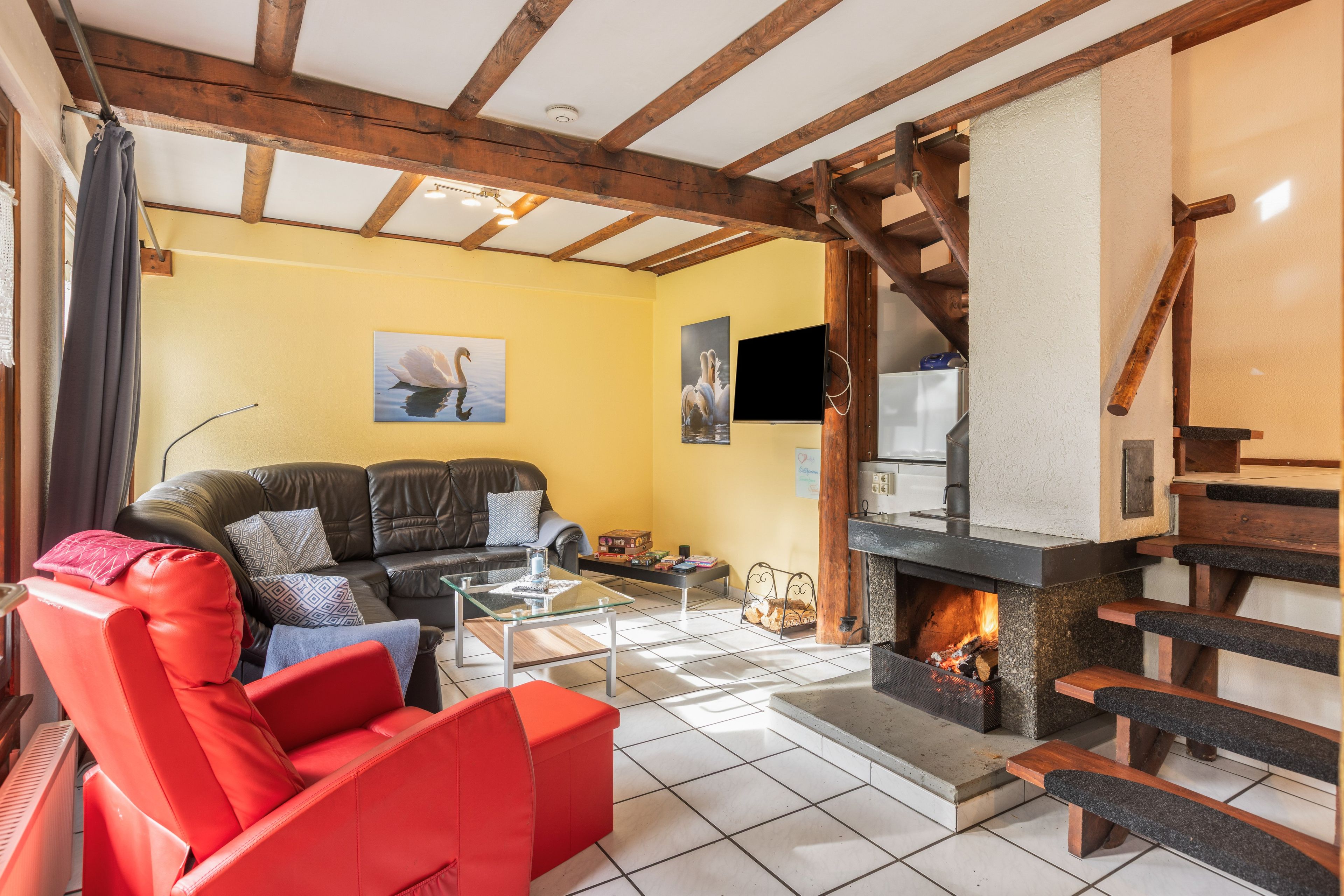 Un salon avec une cheminée, un canapé, un fauteuil rouge et un téléviseur.