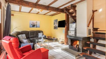 Un salon avec une cheminée, un canapé, un fauteuil rouge et un téléviseur.