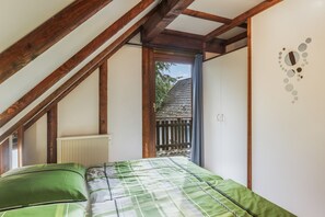 Un dormitorio con techo inclinado, un radiador, una cama con ropa de cama verde y vistas a una valla de madera y árboles desde el exterior.