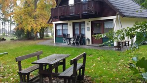 Et toetagers træhus med en balkon, en terrasse med bord og stole, og en have med efterårsblade.
