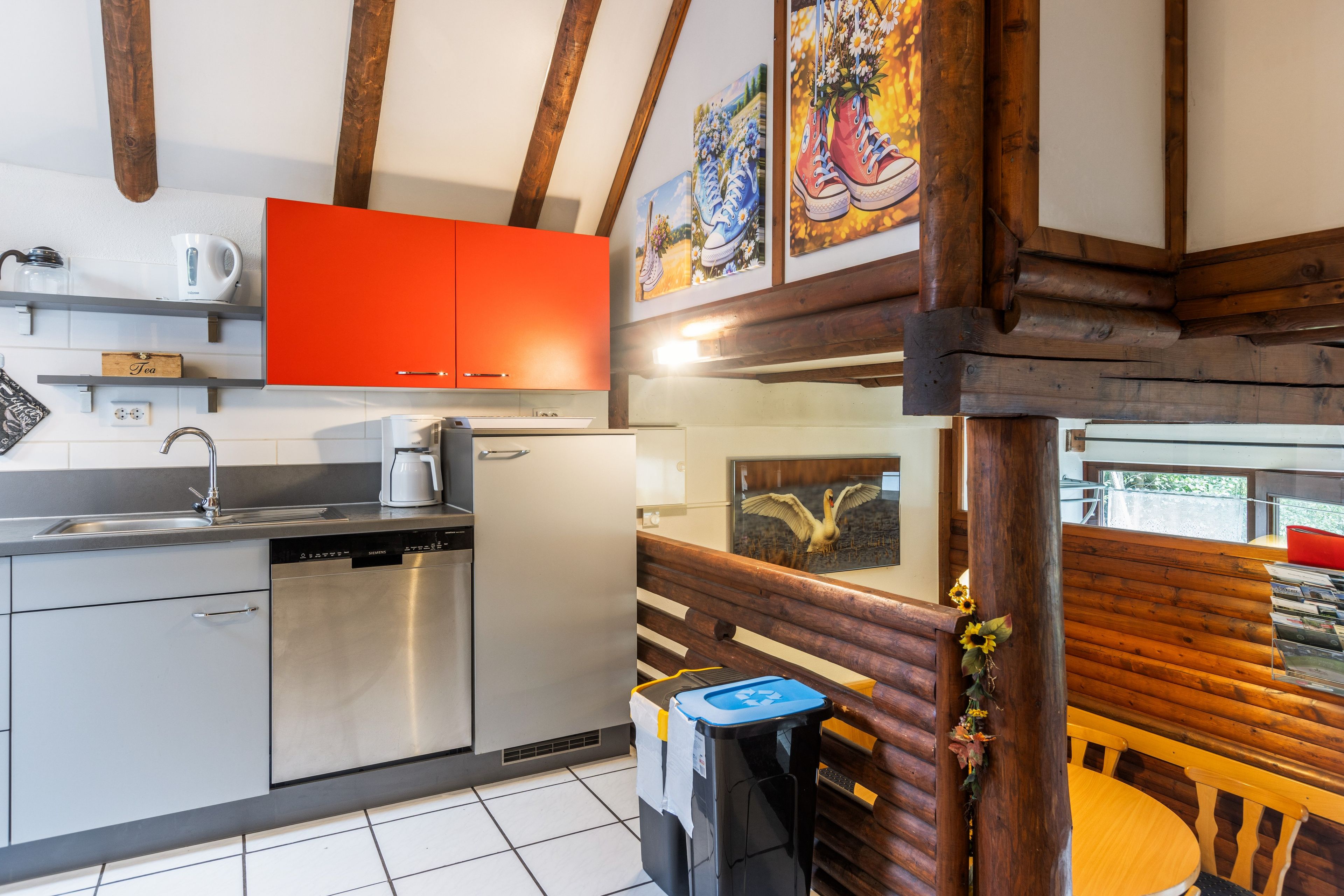 A modern kitchen with stainless steel appliances, a red cabinet, and wooden beams.