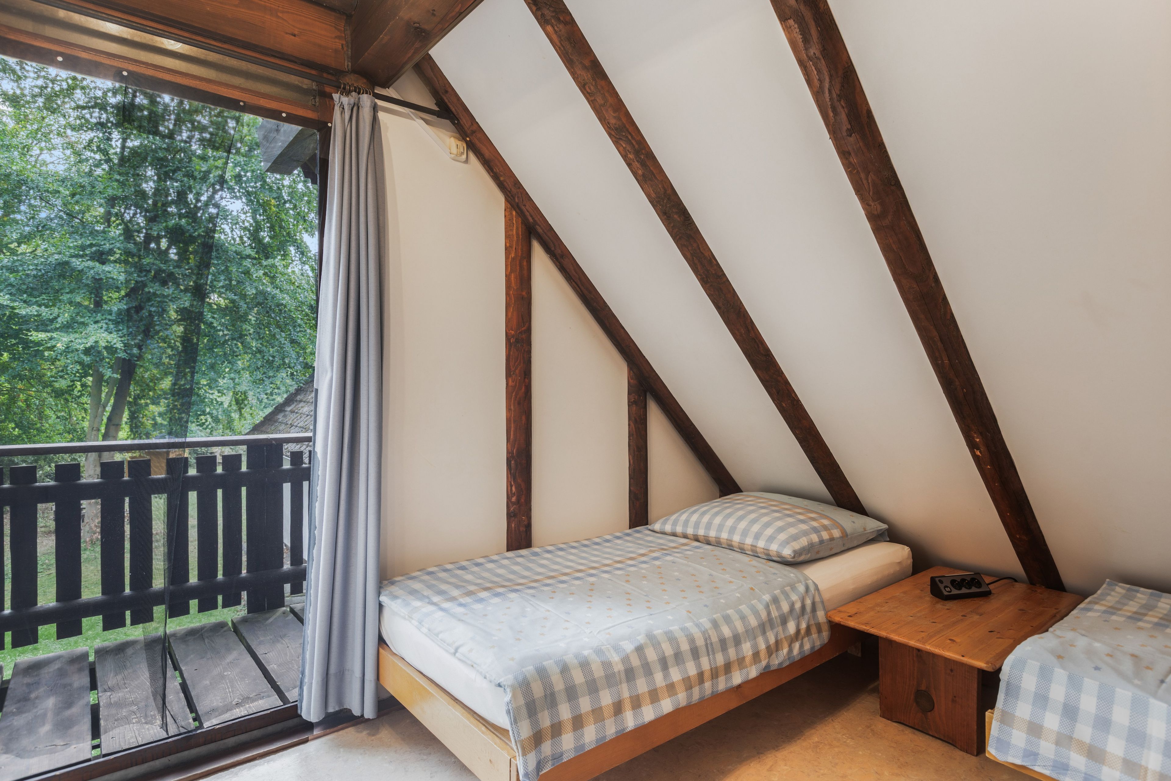 Una camera da letto con soffitto spiovente, un letto con copriletto a scacchi, un comodino e vista sull'esterno.