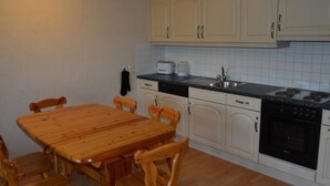 A kitchen with a wooden table and chairs, white cabinets, a black countertop, and a stove. - Anne (Tiefparterre) Appartement/Fewo, Dusche oder Bad, WC 6-Bettwohnung by Interhome (Gstaad)