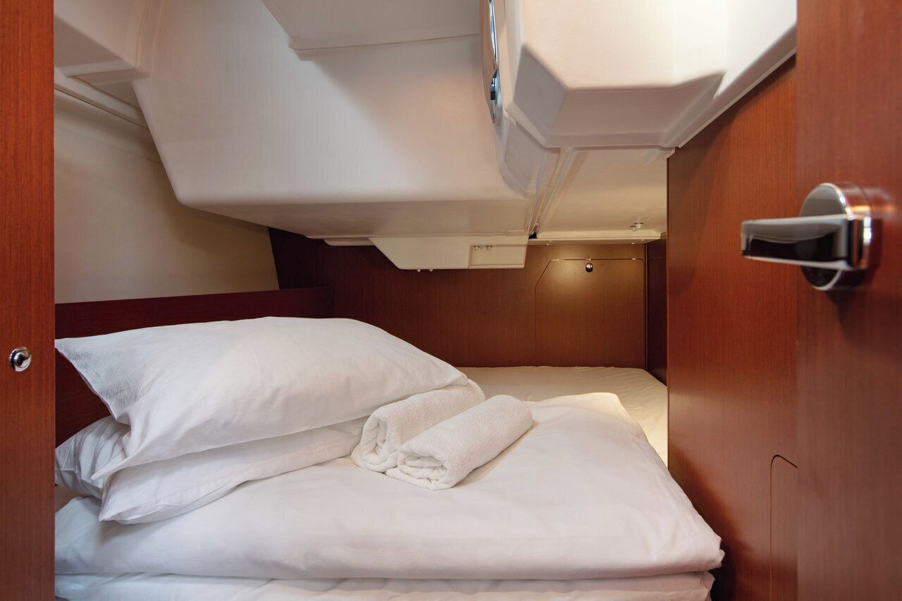 Un lit bien fait, avec du linge de lit blanc et des oreillers, une porte en bois dotée d’une poignée, et un plafond blanc avec un luminaire.