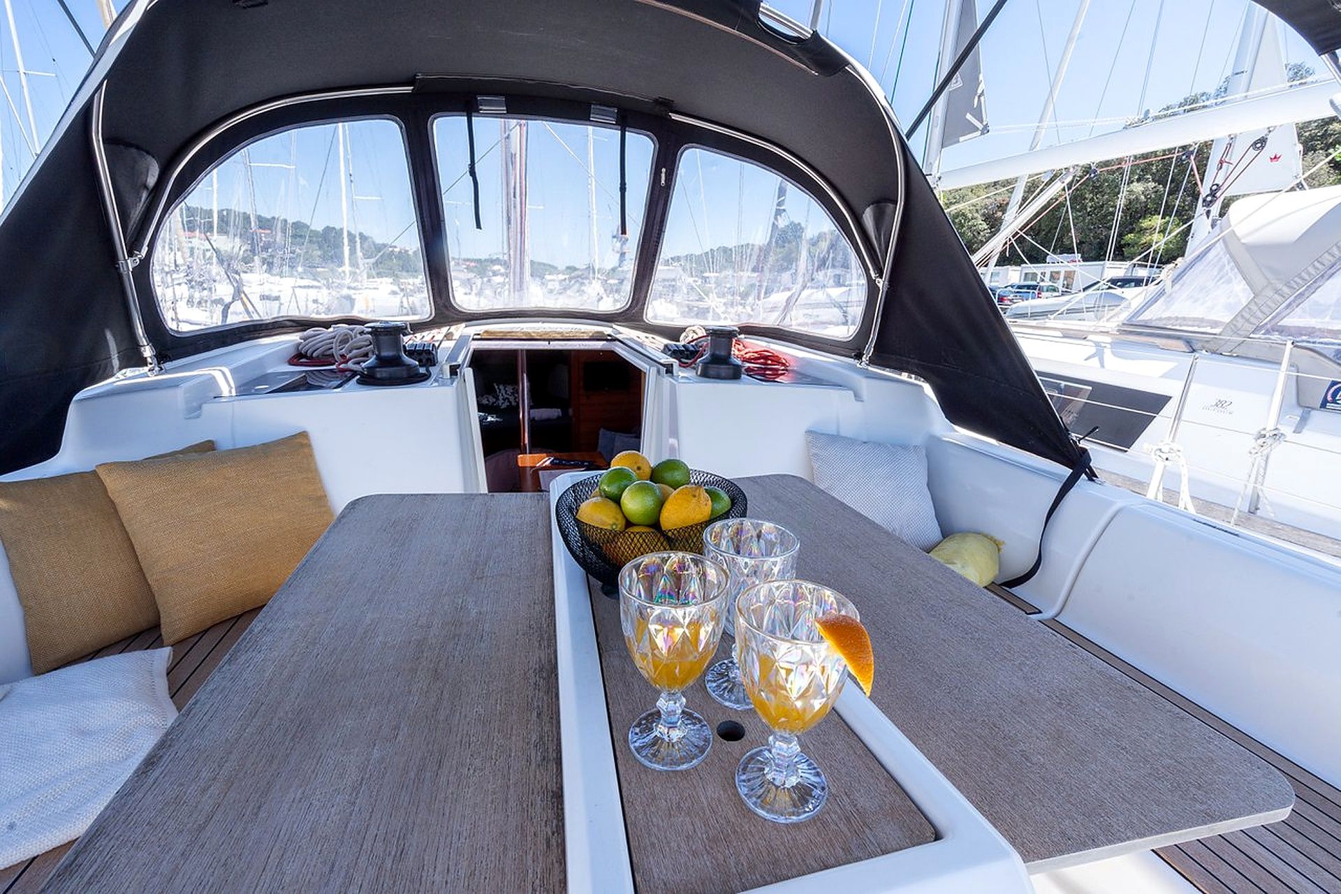 A boat's interior with a dining table set for two, a bowl of fruit, and two glasses of a yellow beverage.
