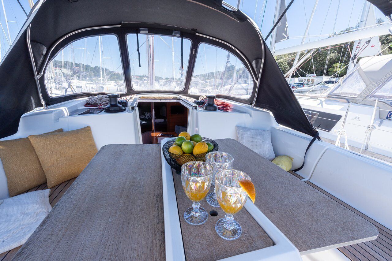 Interior de barco com mesa de jantar, almofadas e cesta de frutas.