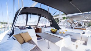 Het dek van een jacht met een eethoek, zitplaatsen en uitzicht op de jachthaven.