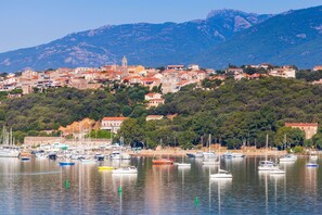 A coastal town with a marina, buildings on a hillside, and mountains in the background.