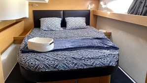 A compact bed with patterned bedding, a bedside table, and a window with curtains. - Sun-Kissed Sailing Adventure in Córcega (Porto-Vecchio)