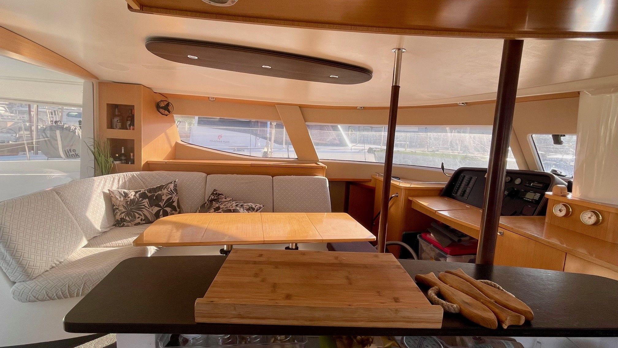 A boat interior with a wooden table, cushioned seating, and a control panel.