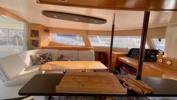 A boat interior with a wooden table, cushioned seating, and a control panel.