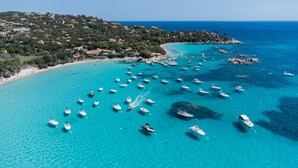 A coastal area with boats on the water, a beach, and a hillside with buildings. - Sun-Kissed Sailing Adventure in Córcega (Porto-Vecchio)
