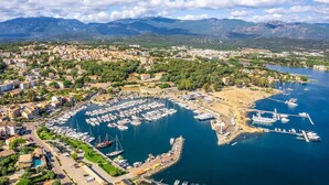 Vue aérienne d’une ville côtière avec un port de plaisance, des zones résidentielles et des montagnes en arrière-plan.