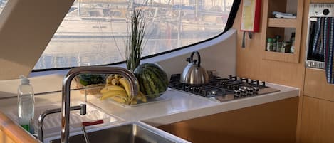 A compact kitchen with a sink, a gas stove, and a window overlooking a marina.