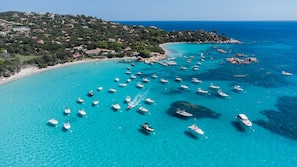 A coastal area with boats on the water, a beach, and a hillside with buildings. - Sun-Kissed Sailing Adventure in Córcega (Porto-Vecchio)
