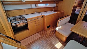 A compact galley with a stove, sink, and storage cabinets, a cushioned seating area, and a small table. - Sun-Kissed Sailing Adventure in Zadar, Croatia (Bibinje)