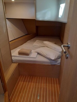 Ein kleines Zimmer mit einem Einzelbett, Holzboden, einem kleinen Nachttisch und einer Tür mit Griff.
