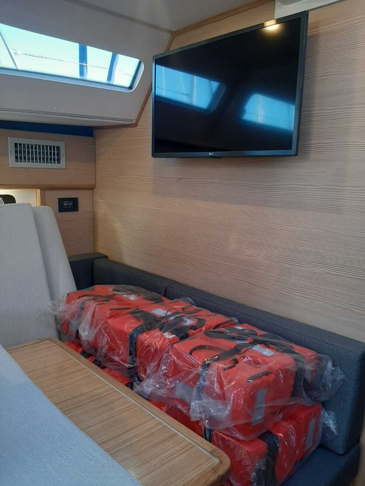 A compact living space with a mounted TV, a cushioned seating area, a table, and a skylight.