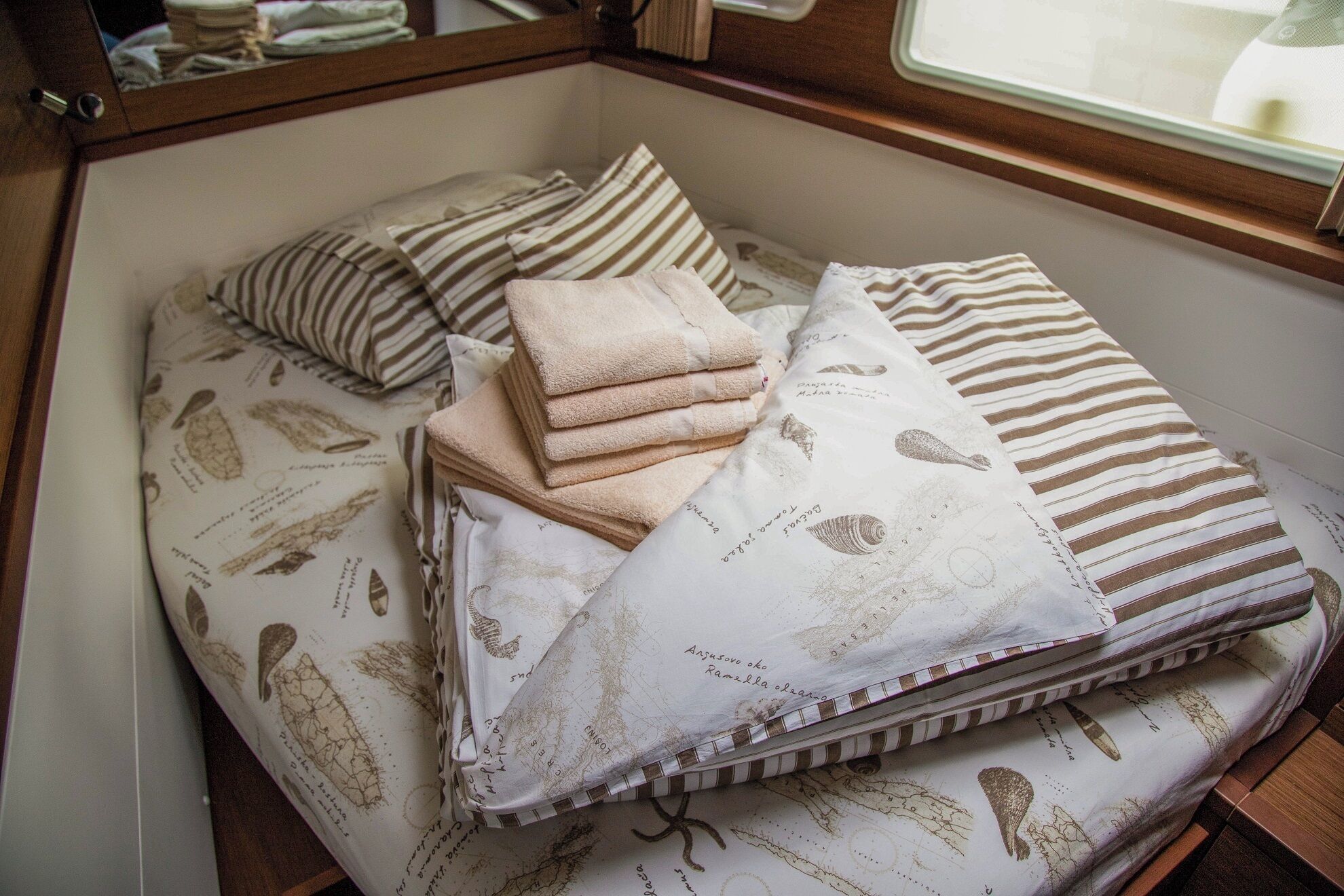 Una cama con ropa de cama a rayas y estampada, una pila de toallas dobladas y una almohada con diseño de mapa.