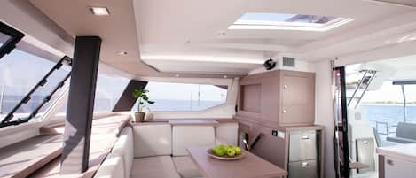 A modern yacht interior with a dining area, seating, and a small kitchen.