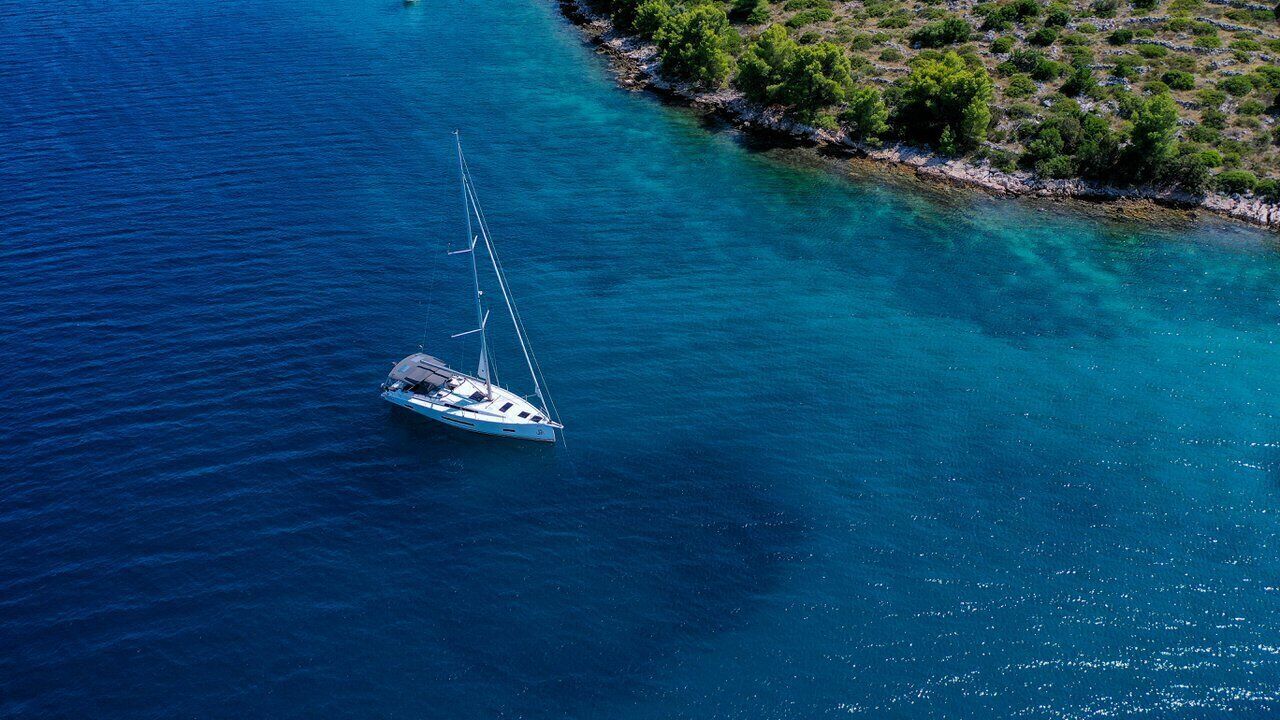 Una barca a vela su acque blu cristalline, vicino a una costa rocciosa con scarsa vegetazione.