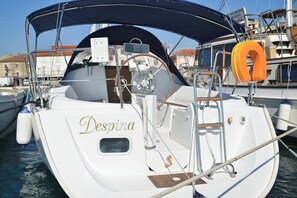 Ein Boot namens 'Despina' liegt in einer Marina festgemacht, mit abgedeckter Cockpit, Steuer und Rettungsring.