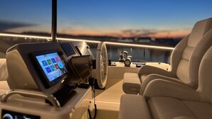 Un poste de pilotage pour bateau, équipé d’un volant, d’un écran numérique et de sièges confortables.