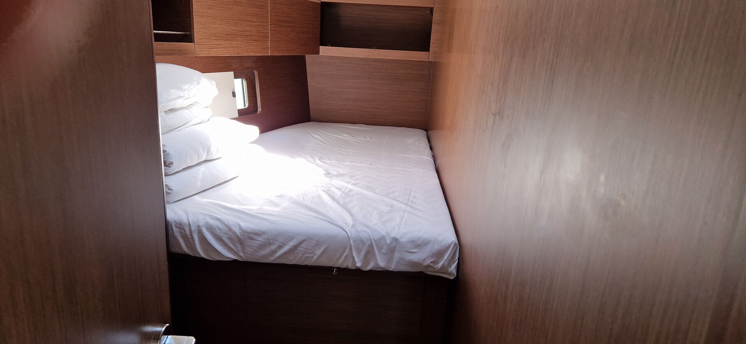 A compact, wooden interior with a bed, pillows, and a small window.