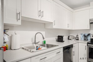 A modern kitchen with white cabinets, a stainless steel sink, a dishwasher, and a microwave. - Modern 2BR Suite Near Lonsdale & Mountains (North Vancouver)
