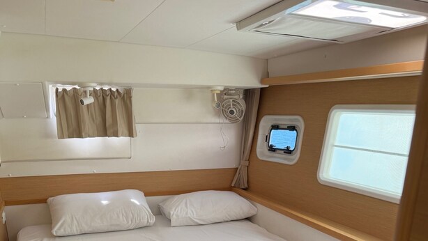 A neatly made bed with white linens and towels, a headboard, a window with curtains, and a small control panel on the wall. - Sun-Kissed Sailing Adventure in Islas Cícladas, Mykonos (Mykonos)