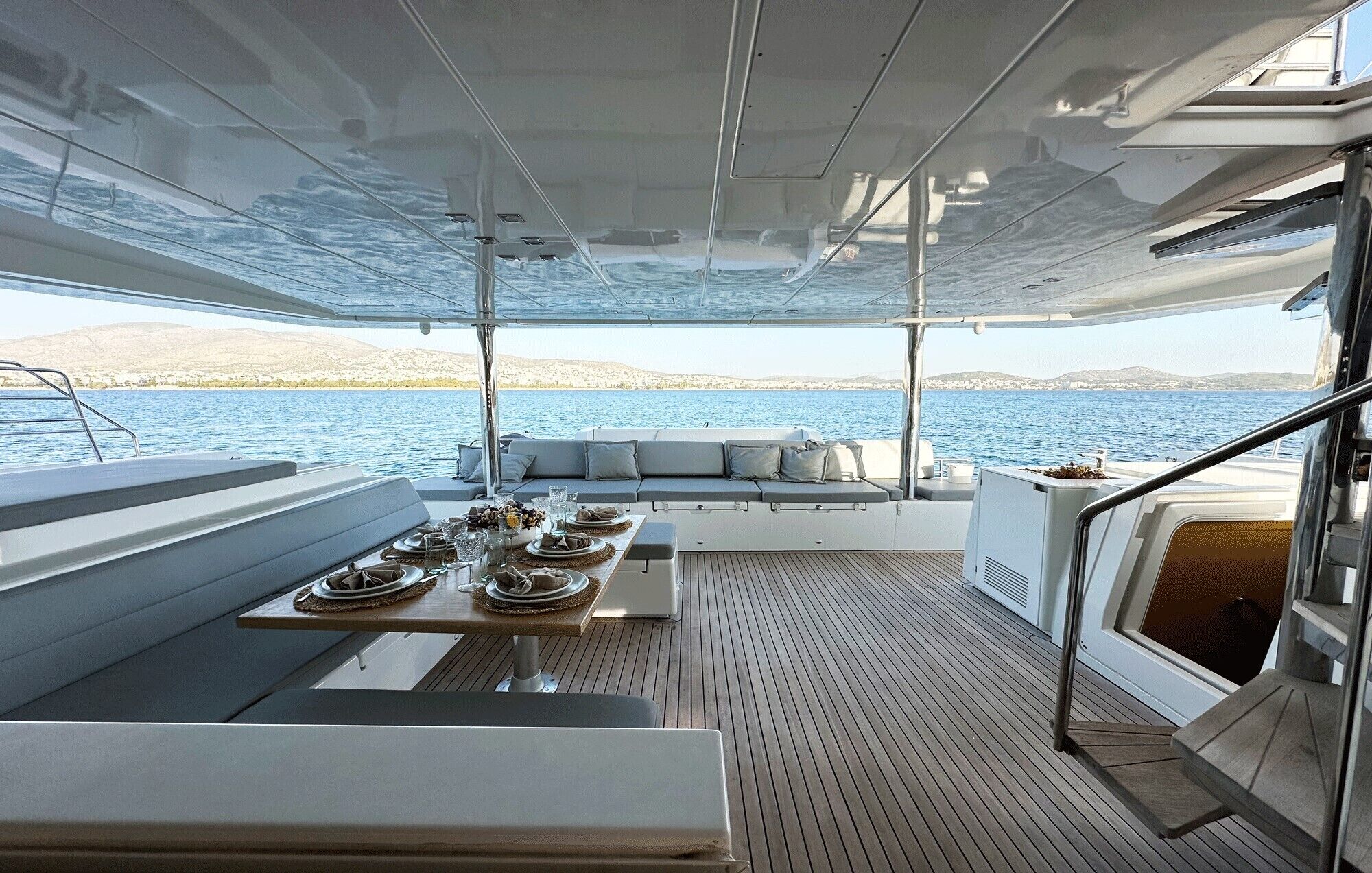 Cubierta de yate con comedor, asientos y vista al mar.