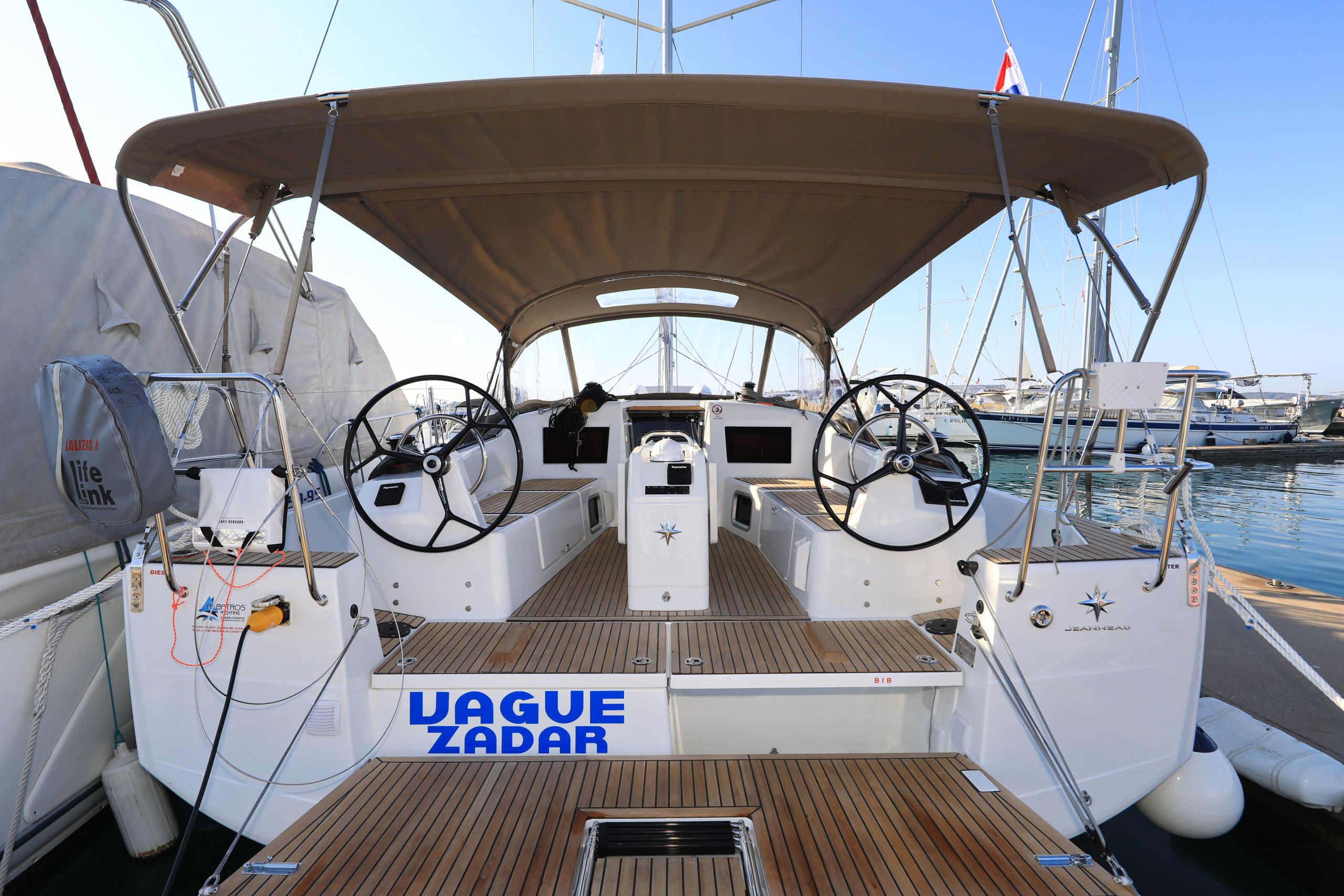 A boat deck with a covered area, steering wheel, and the name 'VAGUE ZADAR' on the side.