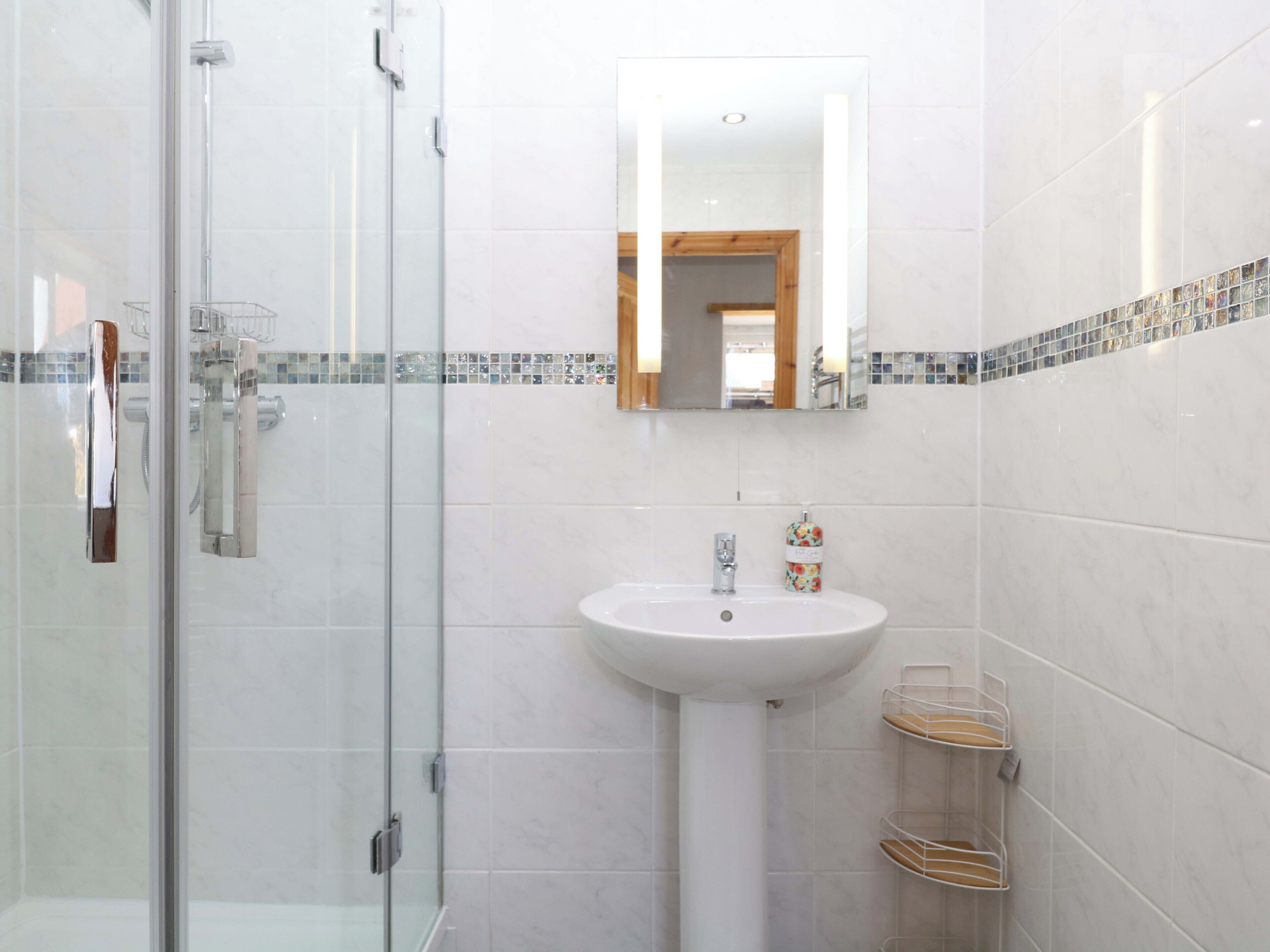 A bathroom with a glass shower enclosure, a white sink, and a mirror.