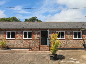 A stone building with a brick facade, a set of stairs leading to a door, and a potted plant in the foreground. - The Milk Shed (Cullompton)