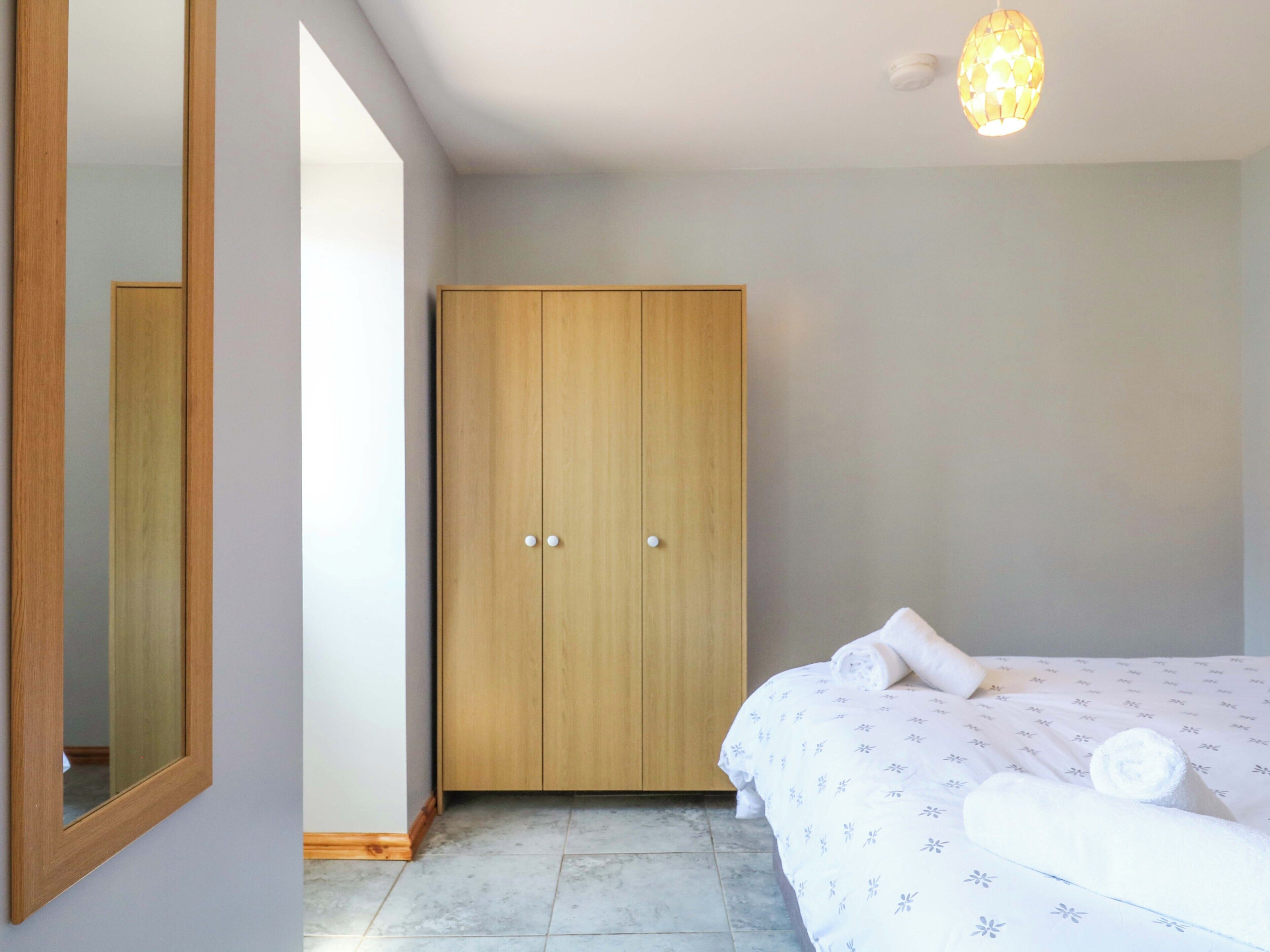 A bedroom with a bed, a wooden wardrobe, a mirror, and a ceiling light fixture.