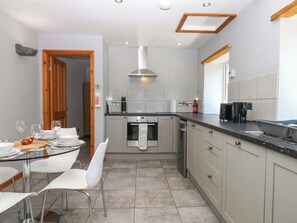 A modern kitchen with a dining area, stainless steel appliances, and a wooden ceiling. - The Milk Shed (Cullompton)