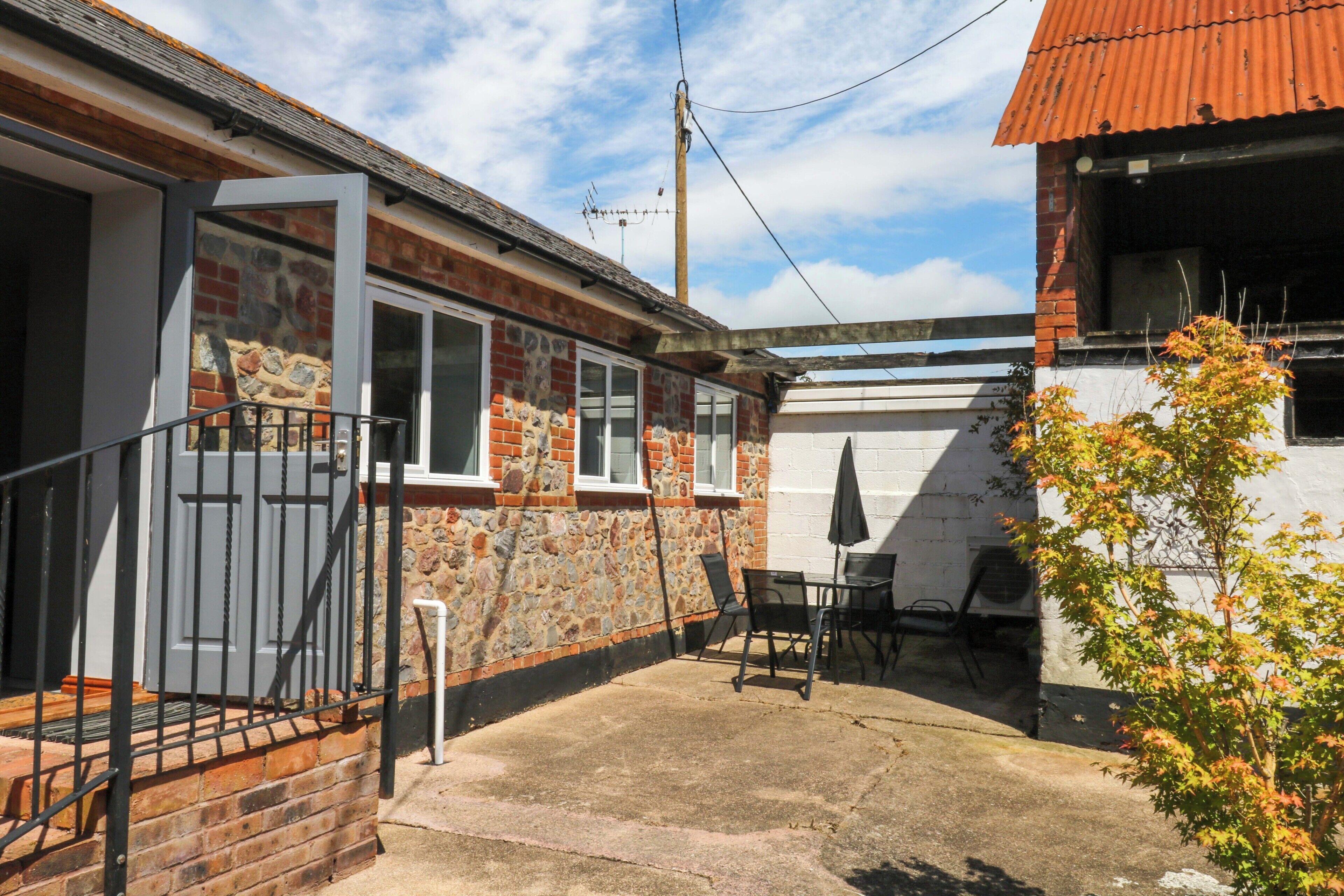 A residential property with a stone facade, a brick chimney, a metal gate, and a patio area with outdoor furniture.