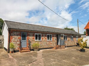 A two-story stone building with a grey roof, a front door, and a small porch with steps. - The Milk Shed (Cullompton)